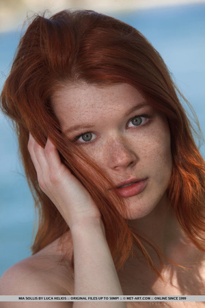 Young redhead takes off her bikini on the shore