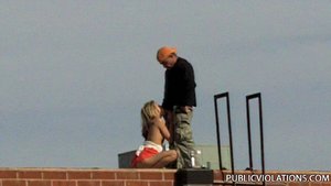 Squatting on a roof top, she pulls his cock out to service it with her moist lips