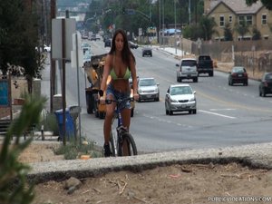 Riding a bike in a bikini top and jean shorts, this brunette whore rides around town