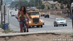 Wearing a lime green bikini top, she rides around the city on a bike