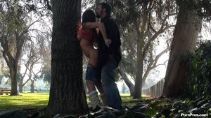 Leaning against a tree, tits exposed, she takes his rod from the back