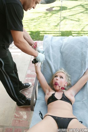Bracing against a tree, this blonde, with a ball gag, gets slammed with a bare cock